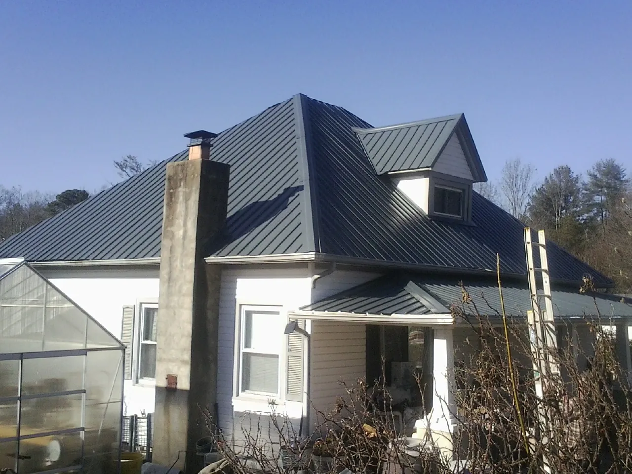 Dark blue standing seam metal roof on a white farmhouse with dormer — Slate & Tile Roof Repair by Roofing Brothers in Rawlins