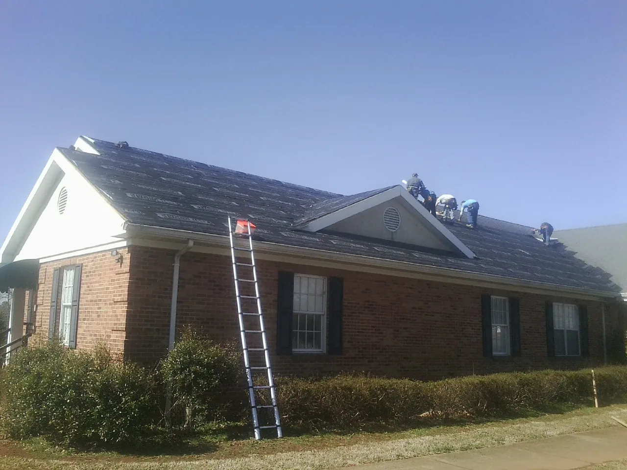 Crew tearing shingles off a brick ranch roof with a ladder set — Emergency Roof Repair work by our crew in Rawlins
