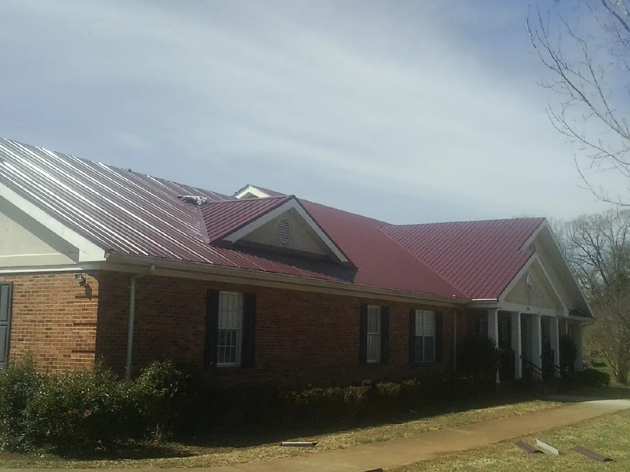 Red metal roof with gabled entries on a long brick building, from a Hail Damage Roof Repair job in Rawlins