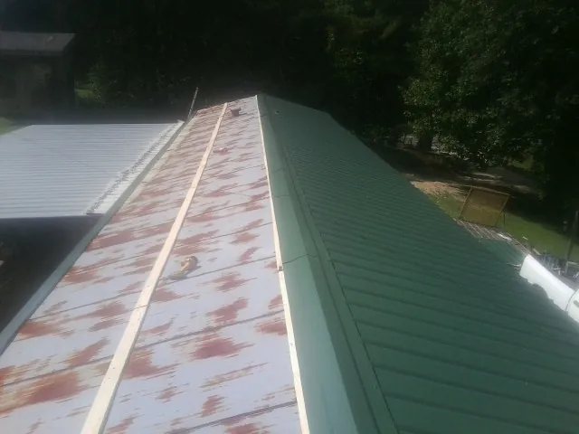 Old rusted panels beside newly installed green metal roofing — Wind Damage Roof Repair by Roofing Brothers in Rawlins