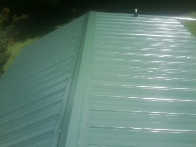 New green metal panels meeting at the ridge of a roof — Flat Roof Repair work by our crew in Rawlins