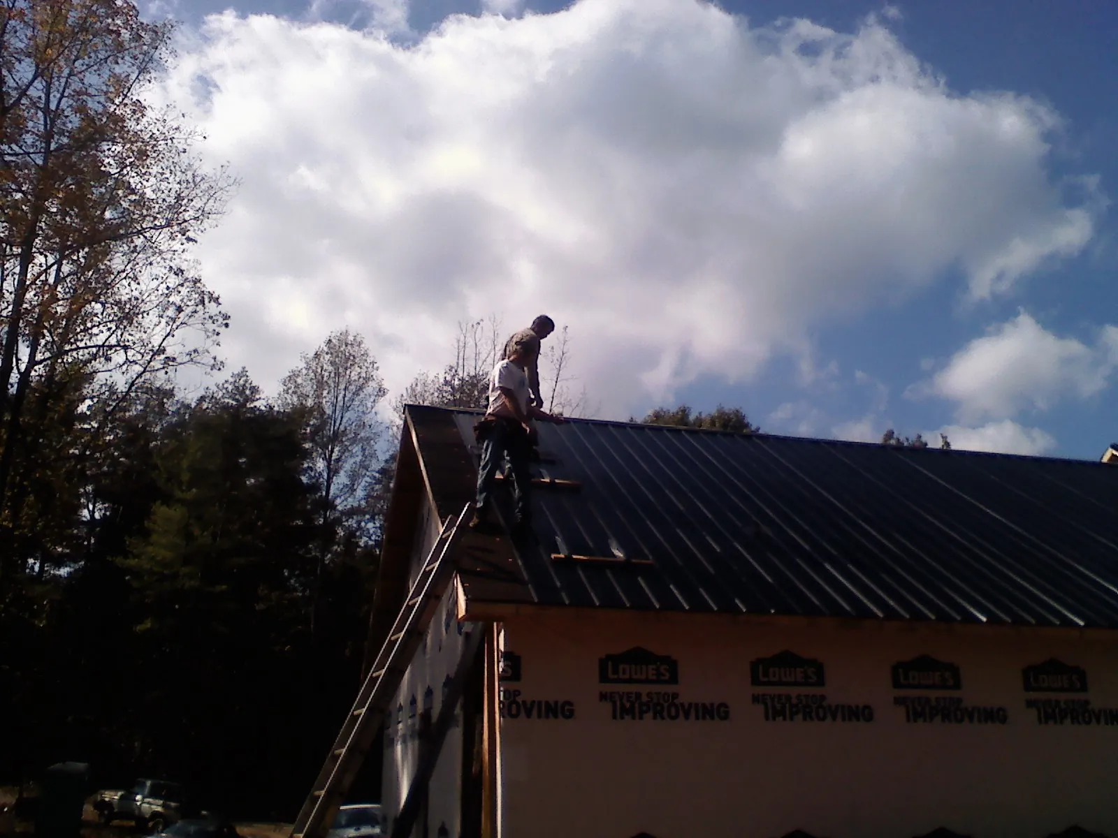 Roofer fastening dark metal panels high against a cloudy sky, from a Roof Inspection job in Rawlins